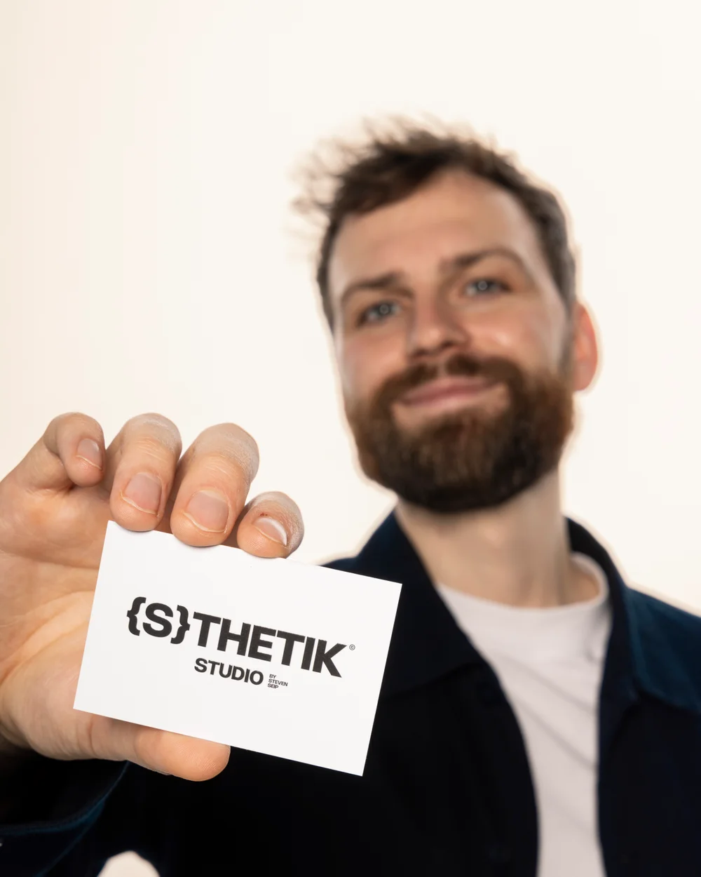 Steven Seip hält eine {S}THETIK STUDIO Visitenkarte