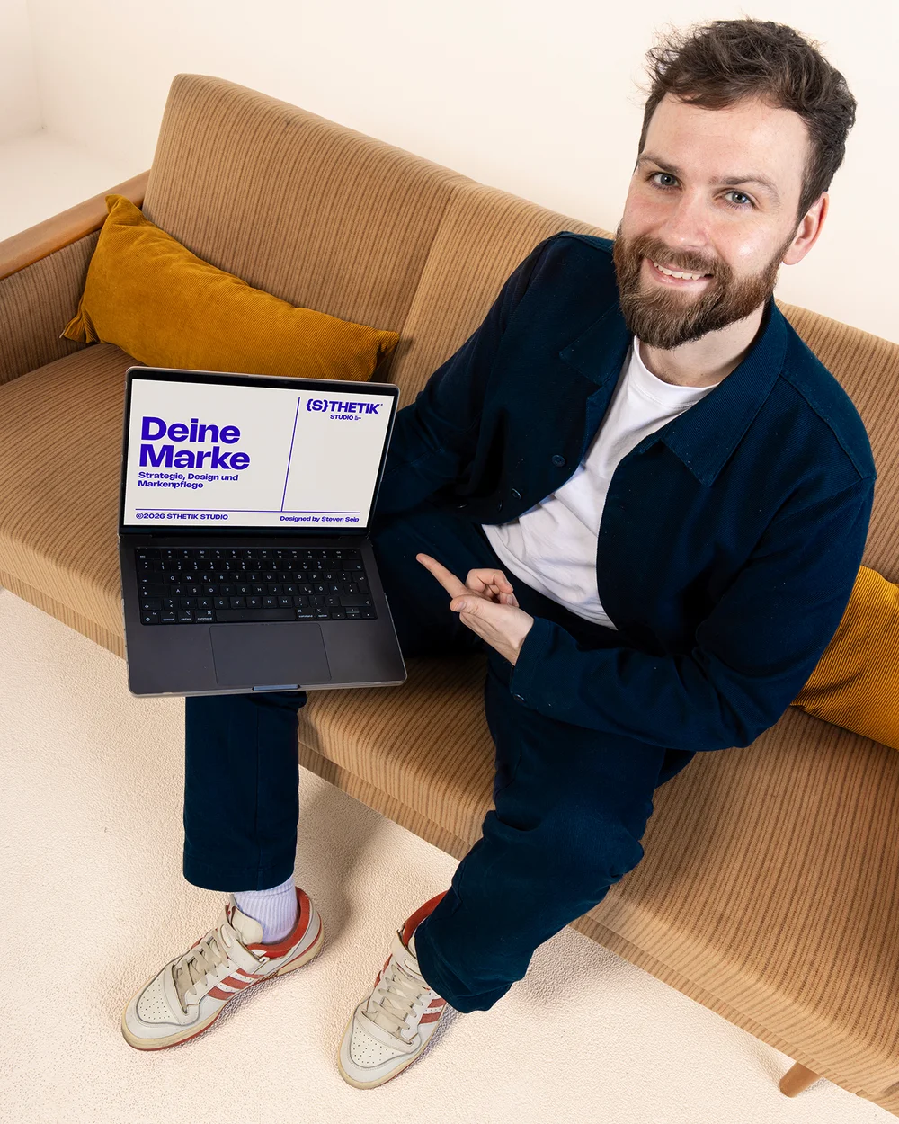 Steven Seip zeigt lächelnd auf einen Laptop-Screen mit dem Slogan Deine Marke